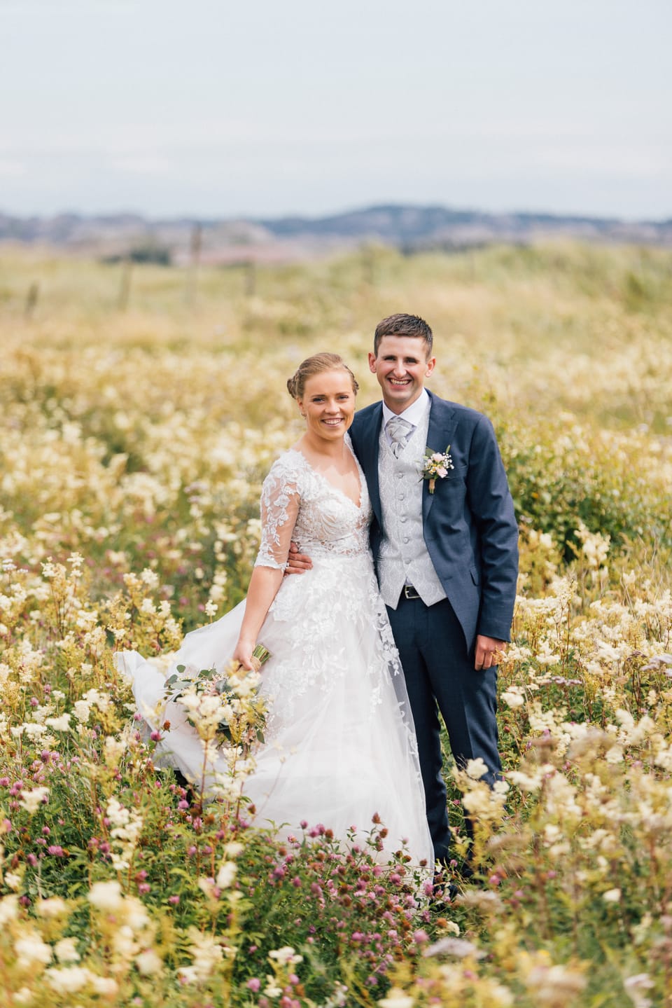 Amalie og Ole Andre går smilende gjennom en blomstereng i fullt sommerflor