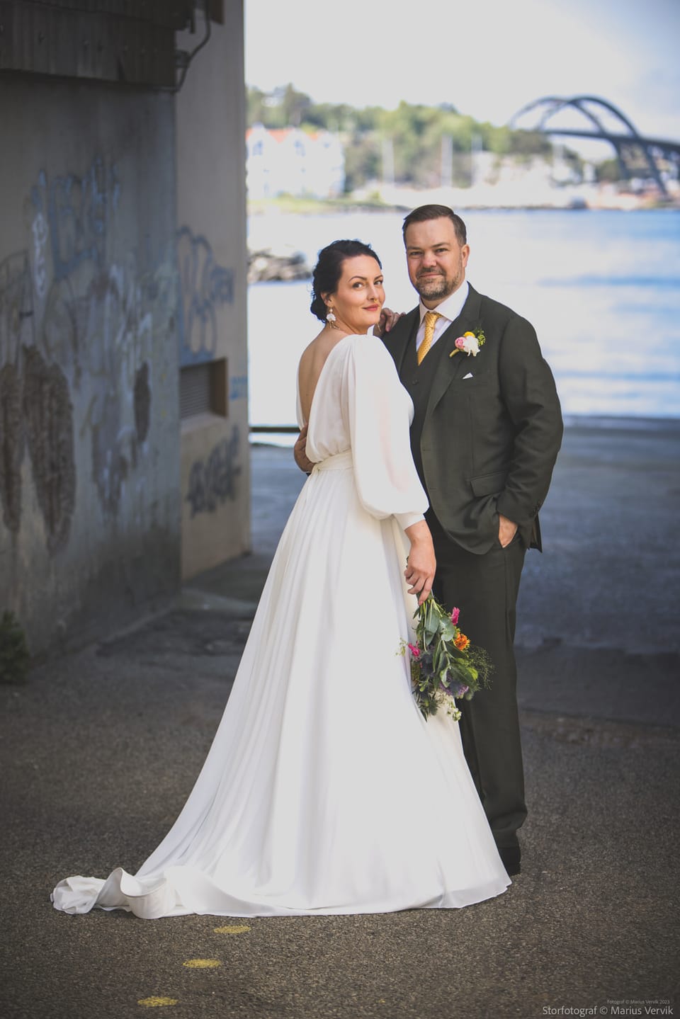 Marie og Steffen ved en rå betongvegg med bybroen i bakgrunnen