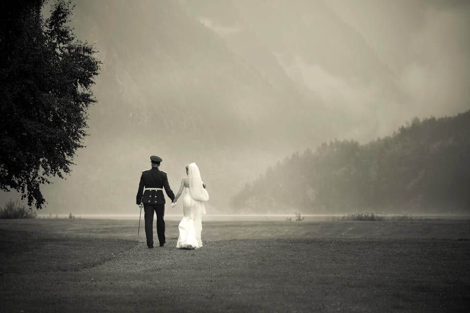 Therese og Yashar går hånd i hånd mot tåkelagt fjell og vann, sort-hvitt